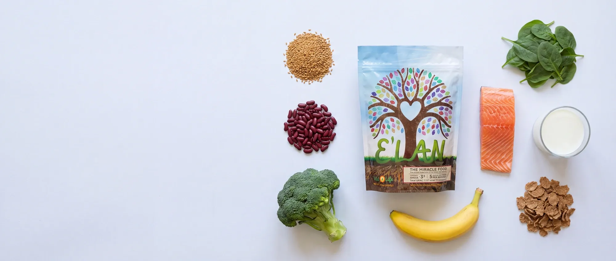 The E'LAN pouch standing on pale paper, surrounded by the foods it is measured against: a pile of golden flax seed, a heap of red kidney beans, a head of broccoli, a handful of spinach leaves, a banana, a raw fillet of wild salmon, a glass of milk and a pile of bran flakes.